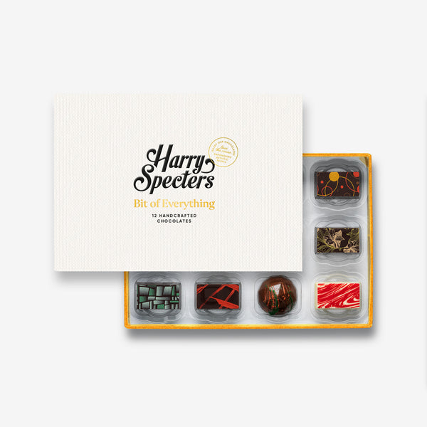 A box of 12 artisan chocolates by Harry Specters including Happy Holidays themed designs partially covered by a box lid 