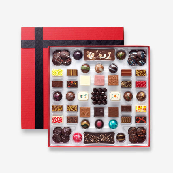 A chocolate box including buttons, bars, and coffee beans colourfully decorated and featuring two good luck chocolates